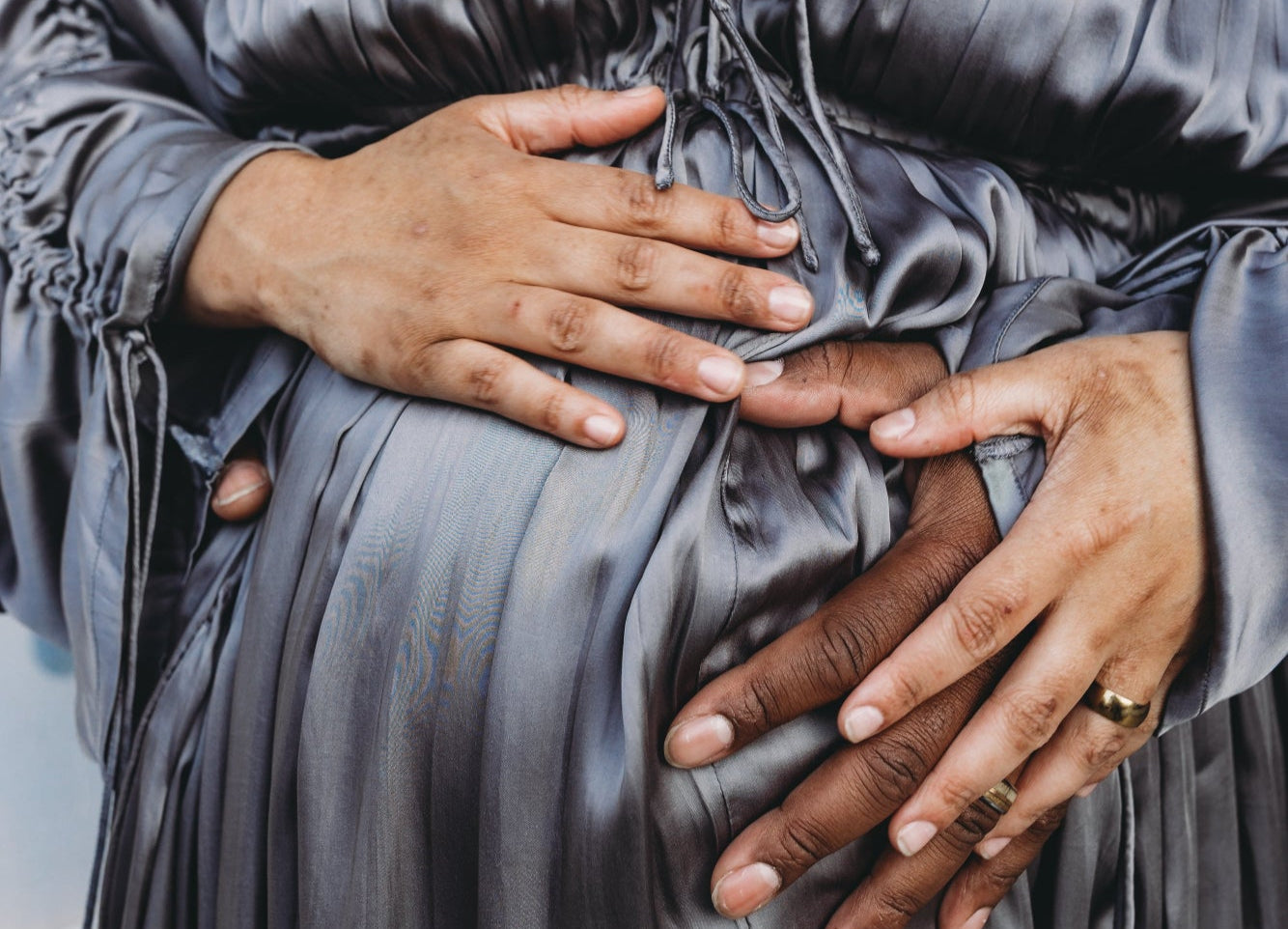 Pregnant mom wearing a gray satin dress with hands on a neutral background